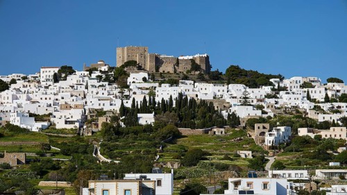 Whitewashed buildings on a green hill with an old castle in the background, Monastery of St John