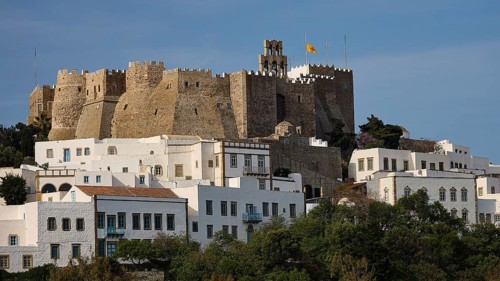 Historic castle on hill with white buildings in the foreground and flag in the sky, Monastery of St
