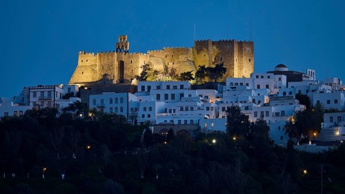 Illuminated castle high above white houses at night, Monastery of St John the Theologian, Monastery