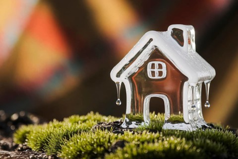 Melting ice sculpture of small house dripping onto moss in warm light, symbolizing climate change