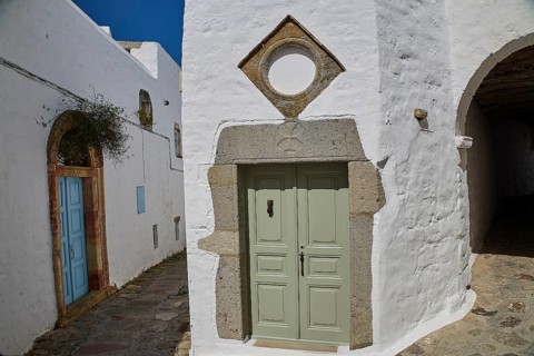 Green door with geometric frame in a white historic building with plants, Mantomata stones, Chora,
