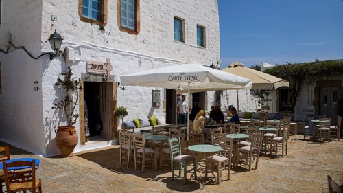 Cosy café terrace with parasols and rustic white buildings in the background, Platia Lesvias,