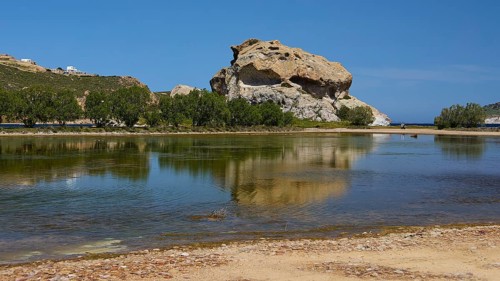 Large rock reflected in a calm lake under a blue sky, Rock of Kalikatsou, Seasonal Salt Lake,