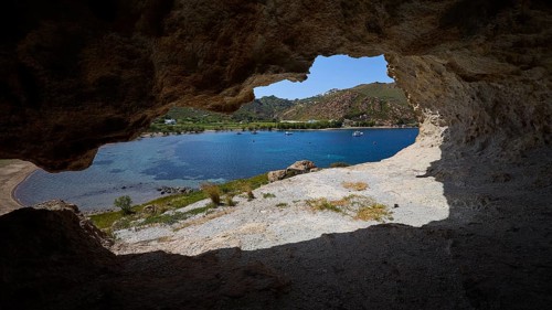 View from a cave onto a blue sea with rocks and coastal landscape in the sunlight, Petra beach,
