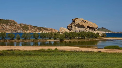 Rock in a lush green landscape with water and trees under a sunny sky, Rock of Kalikatsou, Seasonal