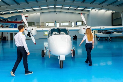 Two pilots walking around a small airplane inside an aircraft hangar, preparing for pre flight