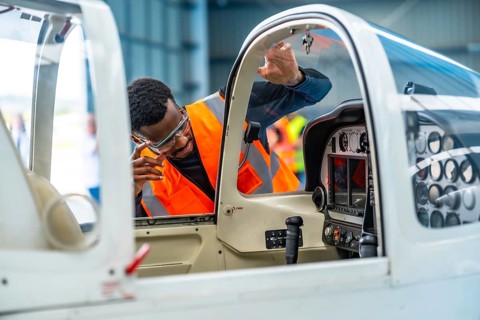 Aircraft engineer wearing safety glasses and a high visibility vest inspects the cockpit of a small