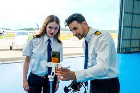 Two pilots are using a smartphone and anemometer to check weather conditions inside an aircraft