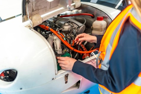 Aircraft mechanic wearing high visibility vest working on airplane engine during maintenance check