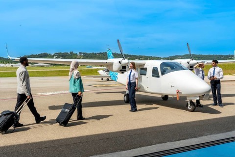 Passengers carrying trolley bags walking towards small airplane and flight crew, ready for boarding