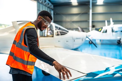 Aircraft maintenance engineer wearing safety glasses and a high visibility vest checks the wing of