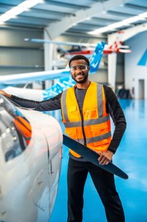Smiling african american aviation engineer holding a propeller blade, performing maintenance checks