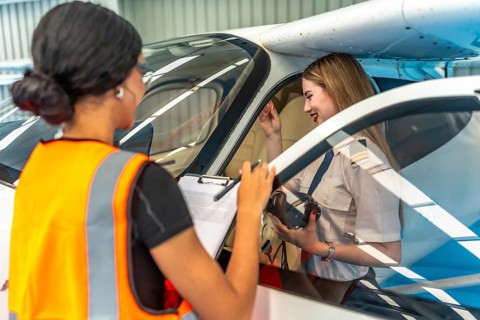 Aircraft maintenance supervisor holding checklist, talking with female pilot sitting in cockpit,