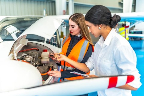 Two female engineers in a hangar inspecting an aircraft engine, focusing on maintenance and safety