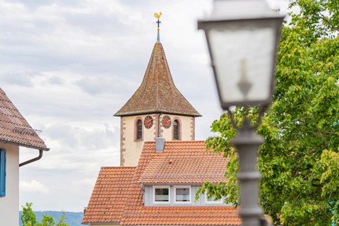 Idyllic view of a church tower with weathercock in the village with blue sky and clouds, family