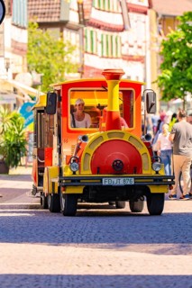 Small colourful train runs through a lively old town with cheerful people, Calw station festival,