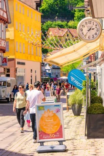 Lively shopping street with cheerful passers-by and colourful decorations on a sunny day, Calw