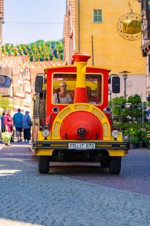 Colourful tourist train runs through a busy street full of people and decorations, Calw station