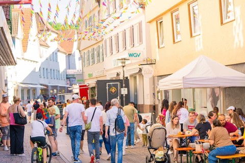 People enjoying a street festival under colourful pennants in an old town, Calw station festival,