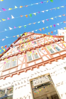 Sunlit half-timbered façade with pennants against a blue sky, Calw railway station festival, Black