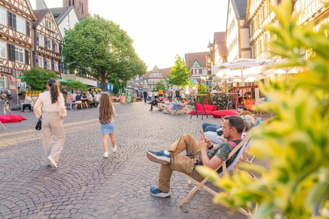 People relaxing on a lively old town square surrounded by historic buildings, Calw railway station