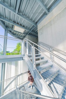 A woman on a modern metal staircase in a light-flooded interior, Zob extension with bridge