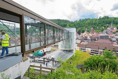 People standing on a modern bridge with a view of a hilly urban landscape, Zob extension with