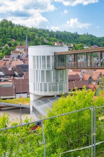 A modern building with a bridge in a town surrounded by green landscape and houses, Zob extension