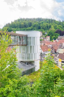 A round modern tower rises above a green, hilly urban landscape, Zob extension with bridge
