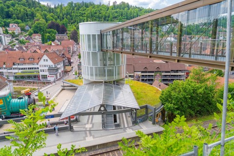 A railway station with a modern glass pedestrian overpass in a small green town, Zob extension with