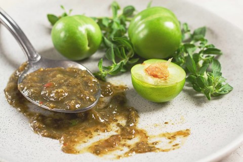 A spoon with tkemali sauce, on a plate, with cherry plum and mint, top view, no people
