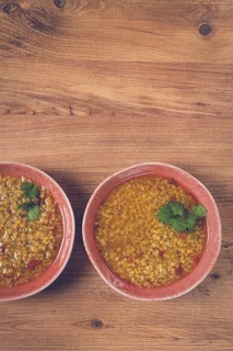 Two bowls of barley stew sit on a wooden table, each garnished with green herbs, capturing the