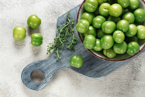 Tkemali, green cherry plum, in a bowl, on a gray table, top view, natural light, no people