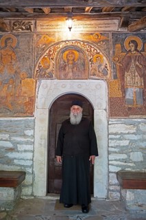 Greek Orthodox priest standing by murals from 1802, Agia Marina church, Kissos, Pelion peninsula,