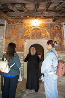 Greek Orthodox priest explains wall paintings from 1802 to visitors, Agia Marina church, Kissos,