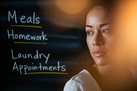 Thoughtful woman in warm light with task-filled blackboard. Concept of mental load, emotional