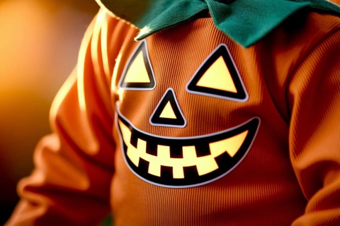 Jack-o'-lantern face on child's pumpkin costume. Concept of Halloween detail, seasonal charm, and