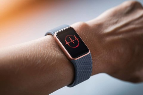 Close-up of wearable health tracker on wrist showing glowing heart rate data in soft, warm light.
