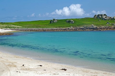 Pristine sandy beach with clear turquoise water and green hill in the background, St Agnes, Isles