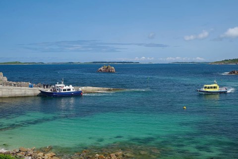 Two boats in the harbour area with a view of the open sea and distant islands under a blue sky, St