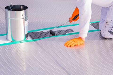 A person applies paint to the floor with a paint roller, next to it a bucket, renewal of the