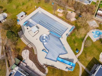 Spacious aerial view of a swimming pool with green areas and several buildings, renovation of the