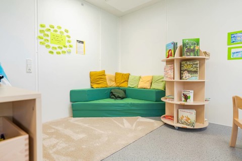 Cosy reading corner in a kindergarten with colourful cushions and books, transitional daycare