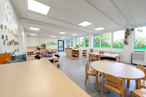 Large, bright nursery room with windows, tables and chairs, wall decorations, transitional