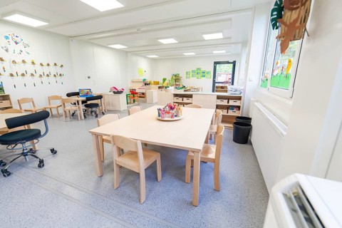 Learning room with tables and chairs, surrounded by bright windows and decorations, transitional