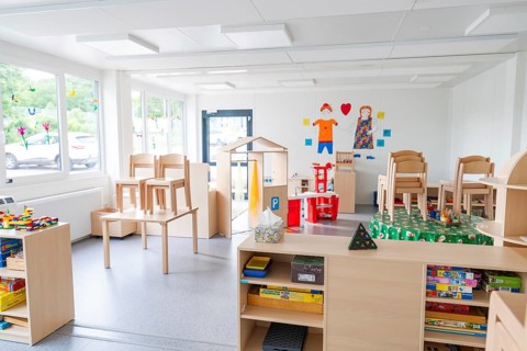 Bright room with toys, set-up chairs and shelves in the foreground, transitional daycare centre in