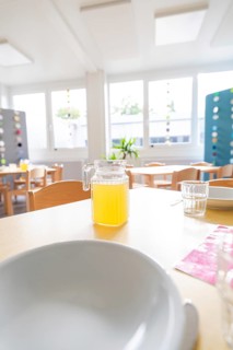 Close-up of a laid table with juice jug and bright window light, transitional daycare centre in