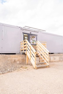 Modern entrance to a grey modular building with wooden stairs, transitional daycare centre in