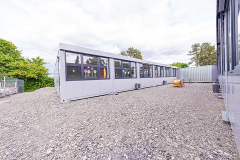 Elongated modern building with large windows and gravel floor, transitional daycare centre in