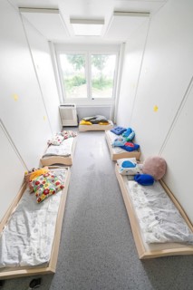 Overview of a dormitory for children with beds, lit by windows, transitional containerised daycare